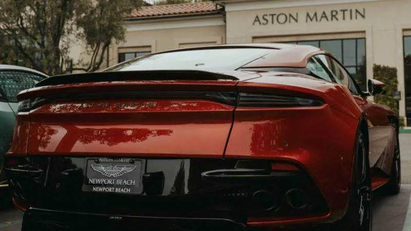 Un Aston Martin rojo aparcado frente a un concesionario, UNSPLASH / JOSHUA_KOBLIN