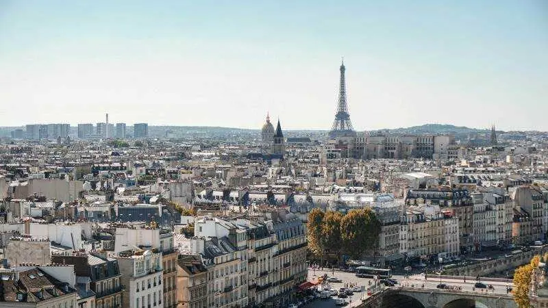 Vista panor&aacute;mica de Par&iacute;s con la Torre Eiffel al fondo, tejados urbanos en primer plano y cielo despejado., UNSPLASH / ALEXANDER KAGAN